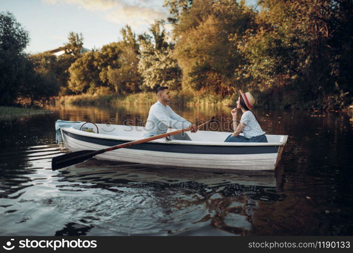 Love couple boating on lake at summer day, water reflection. Romantic data, boat ride, man and woman walking along the river. Love couple boating on lake, water reflection