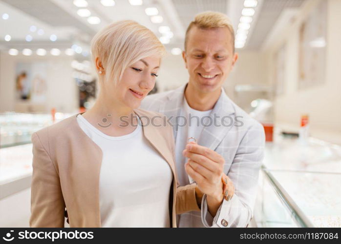 Love couple buying gold decoration. Male and female consumers looking on jewels in jewelry store. Man and woman choosing wedding rings. Future bride and groom in jewellery shop. Couple buying gold decoration in jewellery shop