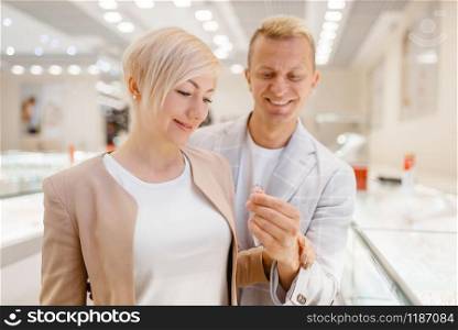 Love couple buying gold decoration. Male and female consumers looking on jewels in jewelry store. Man and woman choosing wedding rings. Future bride and groom in jewellery shop. Couple buying gold decoration in jewellery shop