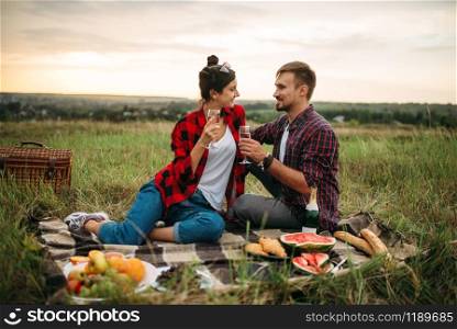 Love couple drinks wine, picnic in summer field. Romantic junket, man and woman leisure together, happy family weekend