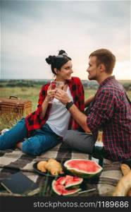 Love couple drinks wine, picnic in summer field. Romantic junket, man and woman leisure together, happy family weekend. Love couple drinks wine, picnic in summer field