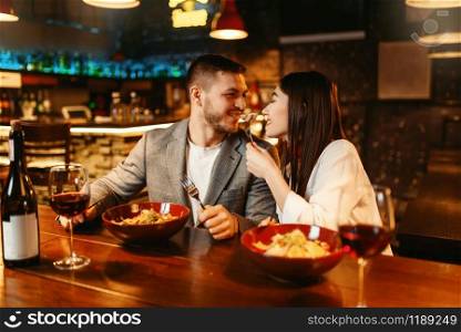 Love couple flirting at wooden bar counter, romantic dinner with paste and red wine. Lovers leisures in pub, husband and wife relaxing together in nightclub
