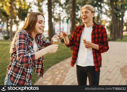 Love couple having fun with ice cream in summer park. Young man and woman leisures with ice-cream, romantic walk together outdoor. Love couple having fun with ice cream in park