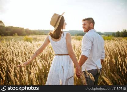 Love couple hold hands, walking in a rye field. Cute family on summer meadow. Love couple hold hands, walking in a rye field