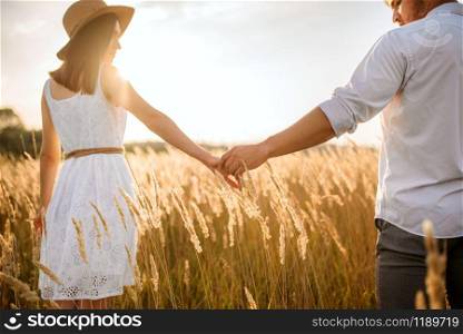 Love couple hold hands, walking in a rye field on sunset. Cute family on summer meadow, happy relationships