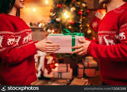 Love couple holding gift box in hands, Christmas celebration. Xmas holidays, happy relationship of man and woman, festive decoration on background. Love couple holding gift box in hands, Christmas
