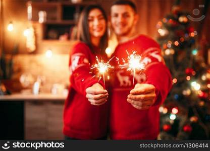Love couple holds sparklers in hands, christmas romantic celebration. Man and woman celebrate xmas together. Love couple holds sparklers in hands, christmas
