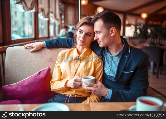 Love couple hugs and looking at the window in restaurant. Man and woman beautiful relationship. Love couple hugs and looking at the window