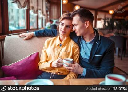 Love couple hugs and looking at the window in restaurant. Man and woman beautiful relationship. Love couple hugs and looking at the window