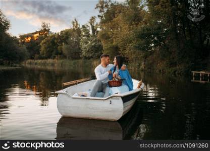 Love couple hugs in a boat on quiet lake at sunset. Romantic meeting, boating trip, man and woman walking along the river. Love couple hugs in a boat on quiet lake at sunset