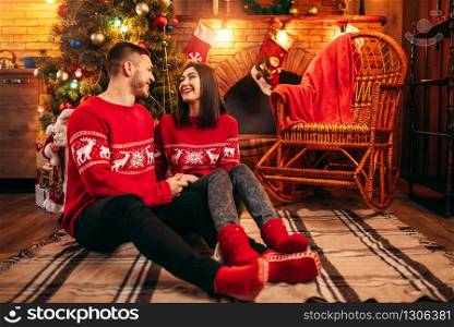 Love couple hugs together, christmas celebration. Xmas holidays, man and woman sitting on the floor, festive decoration on background. Love couple hugs together, christmas celebration
