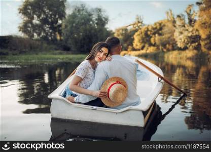 Love couple in boat on quiet lake at summer day. Romantic date, boating trip, man and woman walking along the river. Love couple in boat on quiet lake, romantic date