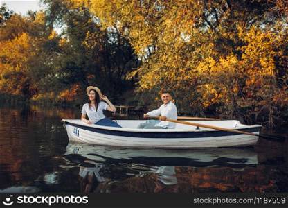 Love couple in boat on quiet lake at summer day, daydream, side view. Romantic date, boating trip, man and woman walking along the river. Love couple in boat on quiet lake, side view