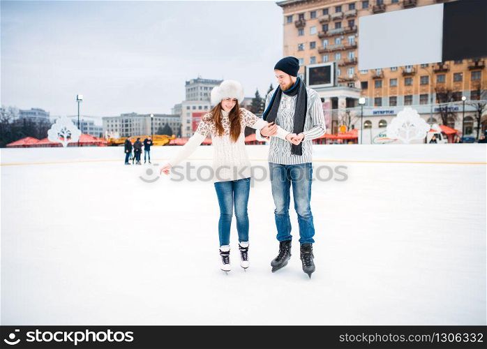 Love couple learn to skate on the rink. Winter skating on open air, active leisure, ice-skating