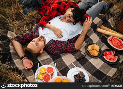 Love couple lies on plaid, picnic in summer field. Romantic junket of man and woman