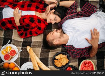 Love couple lies on plaid, top view, picnic in summer field. Romantic junket of man and woman. Love couple lies on plaid, top view