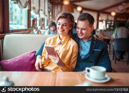 Love couple looks on phone photo album, restaurant on background. Man and woman happy together