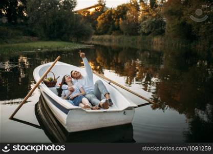 Love couple lying in a boat on quiet lake and dreaming at sunset. Romantic meeting, boating trip, man and woman walking along the river. Love couple lying in a boat and dreaming