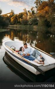 Love couple lying in a boat on quiet lake at summer day at sunset. Romantic meeting, boating trip, man and woman walking along the river. Love couple lying in a boat on lake at sunset
