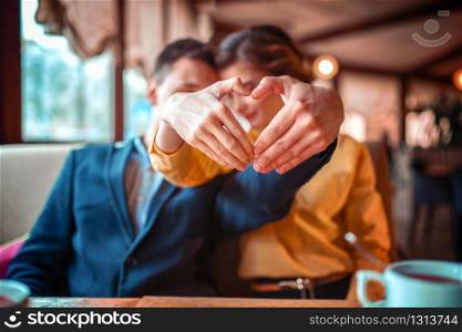 Love couple makes a heart with hands, romantic date in restaurant. Man in suit hugs beautiful woman. Love couple makes a heart with hands