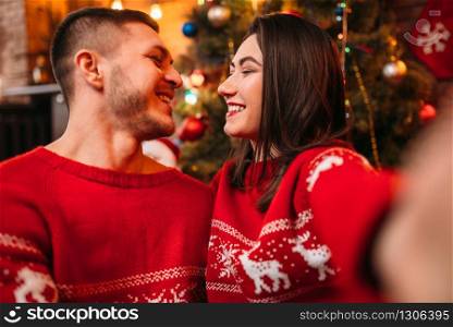 Love couple makes selfie, romantic Christmas celebration. Xmas holidays, happy relationship of man and woman, festive decoration on background. Love couple makes selfie, Christmas celebration