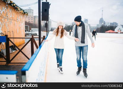 Love couple, man learn woman to skate on the rink. Winter skating on open air, active leisure, ice-skating