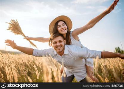 Love couple playing in wheat field at sunny day. Pretty wife and husband walking on summer meadow