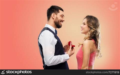 love, couple, proposal and people concept - happy man giving diamond engagement ring in little red box to woman over living coral background. man giving woman engagement ring on valentines day