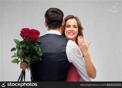 love, couple, proposal and people concept - happy woman with engagement ring and bunch of roses hugging man over grey background. woman with engagement ring and roses hugging man