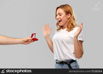 love, couple, proposal and people concept - man giving diamond engagement ring in little red box to happy woman over grey background. man giving woman engagement ring on valentines day