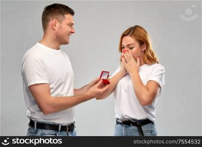 love, couple, proposal and people concept - man giving diamond engagement ring in little red box to happy woman over grey background. man giving woman engagement ring on valentines day