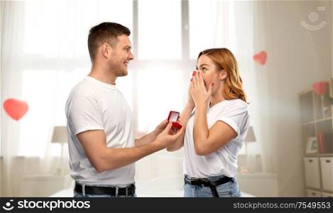 love, couple, proposal and valentine&rsquo;s day concept - man giving diamond engagement ring in little red box to happy woman over bedroom decorated with heart shaped balloons background. man giving woman engagement ring on valentines day