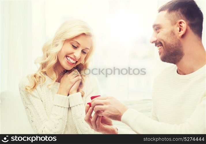 love, couple, relationship, proposal and holidays concept - happy man giving engagement ring in little red gift box to woman at home. happy man giving engagement ring to woman at home