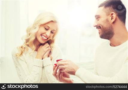 love, couple, relationship, proposal and holidays concept - happy man giving engagement ring in little red gift box to woman at home. happy man giving engagement ring to woman at home