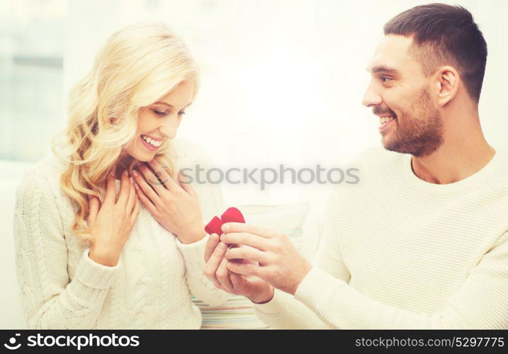 love, couple, relationship, proposal and holidays concept - happy man giving engagement ring in little red gift box to woman at home. happy man giving engagement ring to woman at home