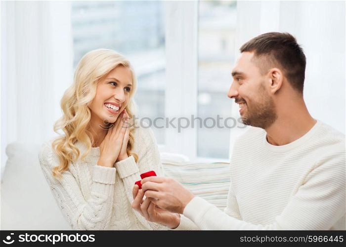 love, couple, relationship, proposal and holidays concept - happy man giving engagement ring in little red gift box to woman at home
