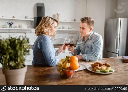 Love couple sitting at the table, romantic dinner. Man and woman drinks wine and eats fruits on the kitchen. Happy lifestyle, beautiful relationship. Love couple sitting at the table, romantic dinner