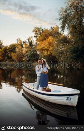 Love couple standing in a boat on quiet lake at summer day on sunset. Romantic meeting, boating trip, man and woman walking along the lake. Love couple standing in a boat on quiet lake
