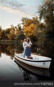 Love couple standing in a boat on quiet lake at summer day on sunset. Romantic meeting, boating trip, man and woman walking along the lake. Love couple standing in a boat on quiet lake