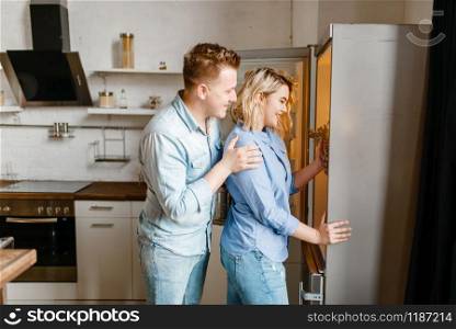 Love couple takes out the fruit from the fridge, romantic dinner preparation. Man and woman cooking on the kitchen together. Happy lifestyle, beautiful relationship