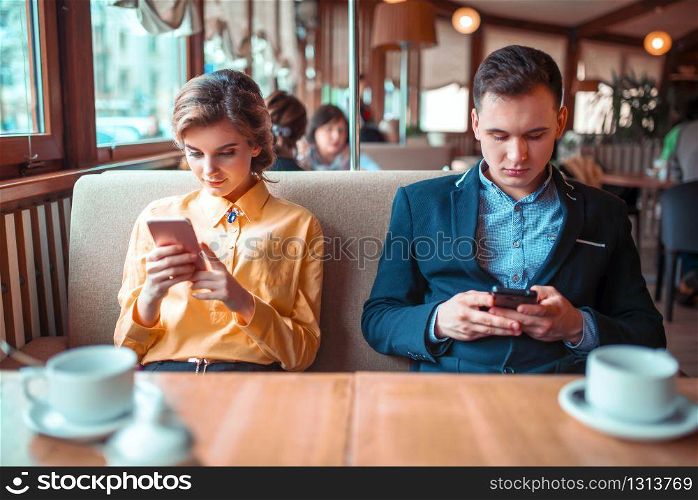 Love couple use their mobile phones in restaurant. Man and woman on romantic date