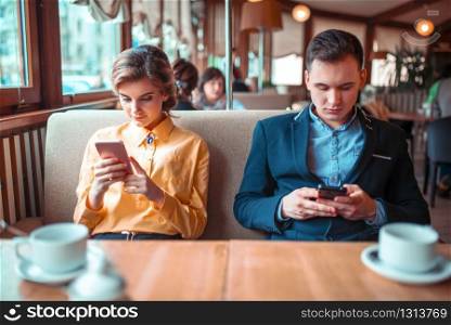 Love couple use their mobile phones in restaurant. Man and woman on romantic date