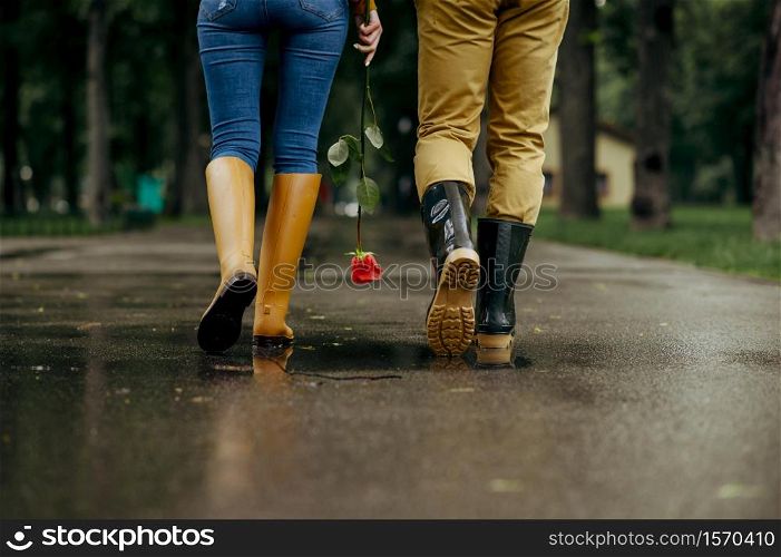 Love couple walks in park, summer rainy day. Man and woman leisures together, romantic date on walking path, wet weather in alley. Love couple walks in park, summer rainy day