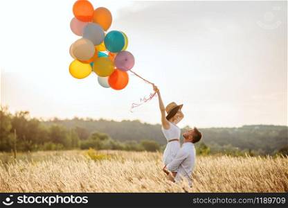 Love couple with balloons hugs in a rye field. Pretty woman on summer meadow