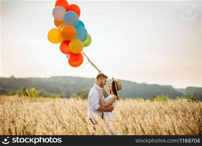 Love couple with colorful air balloons in a rye field. Pretty woman on summer meadow. Love couple with colorful balloons in a rye field