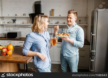 Love couple with croissants and cookies, romantic breakfast. Man and woman eats dessert on the kitchen, good morning. Happy lifestyle, beautiful relationship