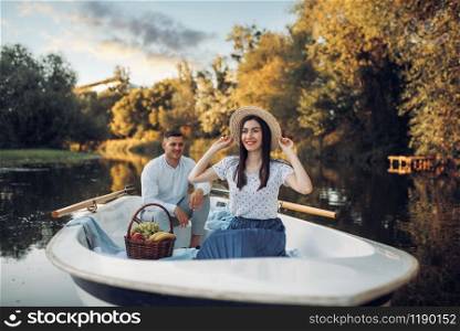 Love couple with fruit basket in boat on quiet lake at summer day. Romantic date, boating trip, man and woman walking along the river. Love couple with fruit basket in boat