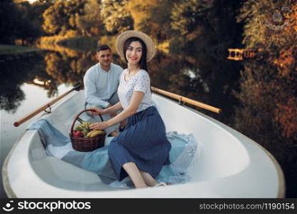 Love couple with fruit basket in boat on quiet lake at summer day. Romantic date, boating trip, man and woman walking along the river. Love couple with fruit basket in boat