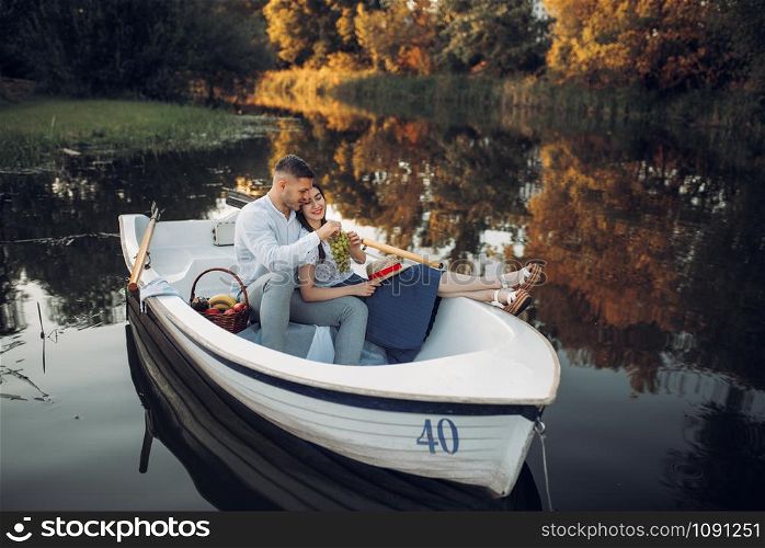 Love couple with fruit basket lying in a boat on quiet lake at summer day. Romantic meeting, boating trip, man and woman walking along the river. Love couple with fruit basket lying in a boat