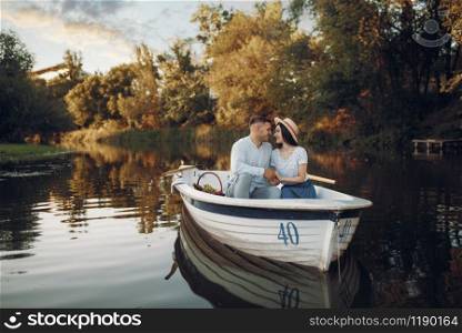 Love couple with fruit basket, relaxing in boat on quiet lake at summer day. Romantic date, boating trip, man and woman walking along the river. Love couple with fruit basket, relaxing in boat